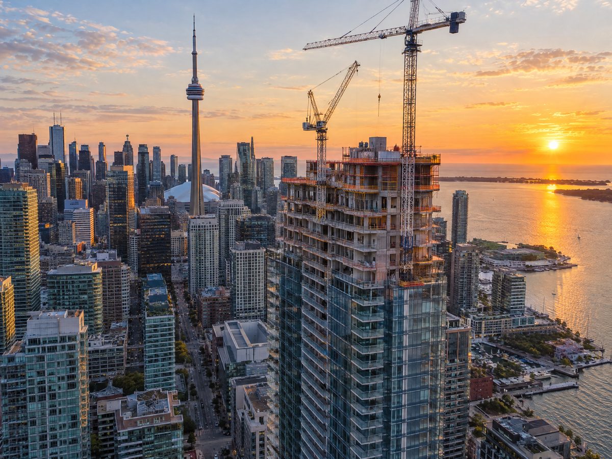 Aerial view of a glass condo tower under construction with cranes in downtown Toronto, CN Tower behind