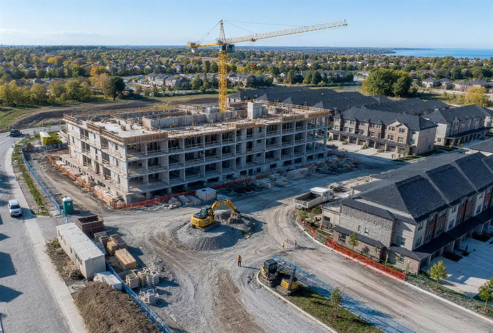 Aerial view of a mid-rise building under construction with a tower crane, beside new townhomes