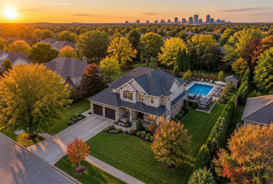 Aerial view of a two-storey home with a backyard pool among autumn trees at golden hour
