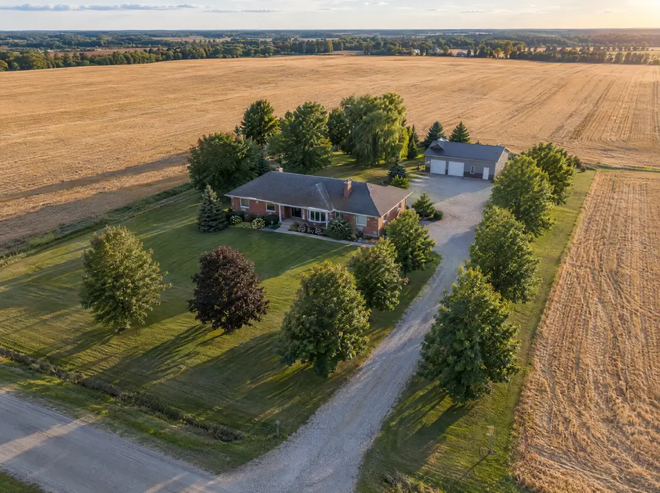 Aerial view of a rural brick bungalow on a tree-lined lot surrounded by golden farm fields