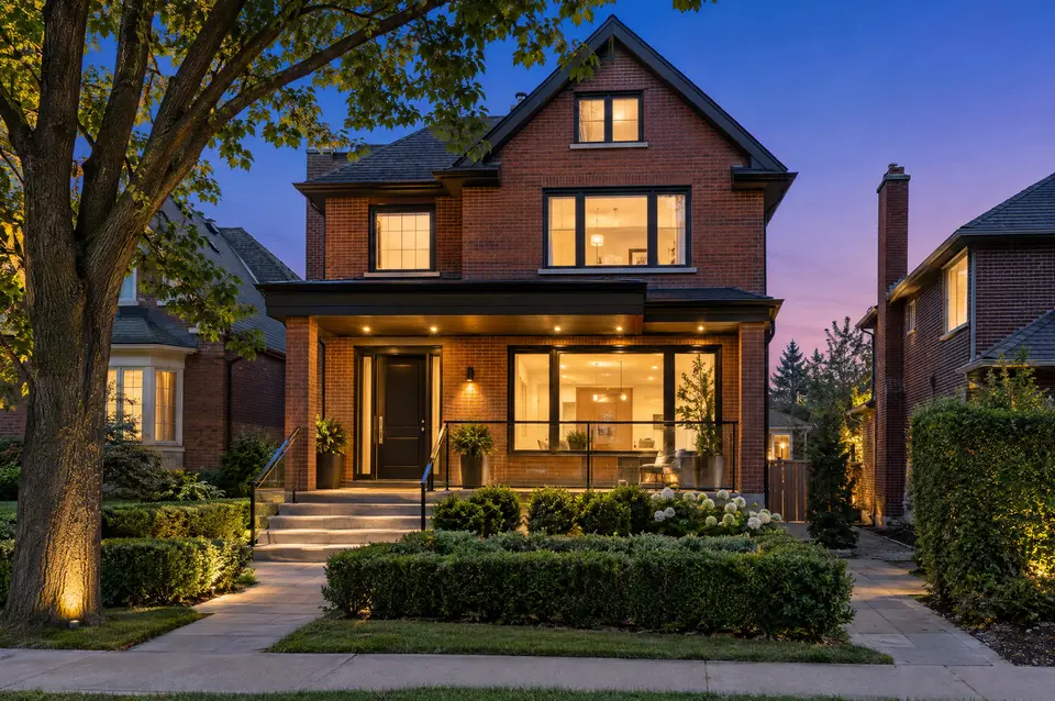 Red-brick two-storey home with warm interior lights and landscaped front steps at dusk