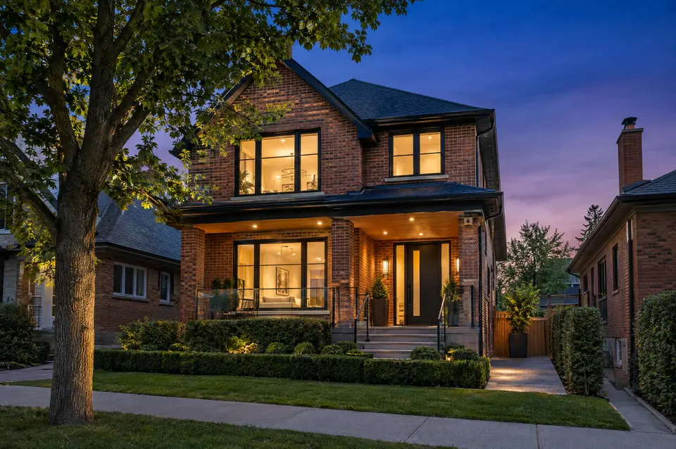 Brick infill home with large lit windows and landscaped front walk at dusk