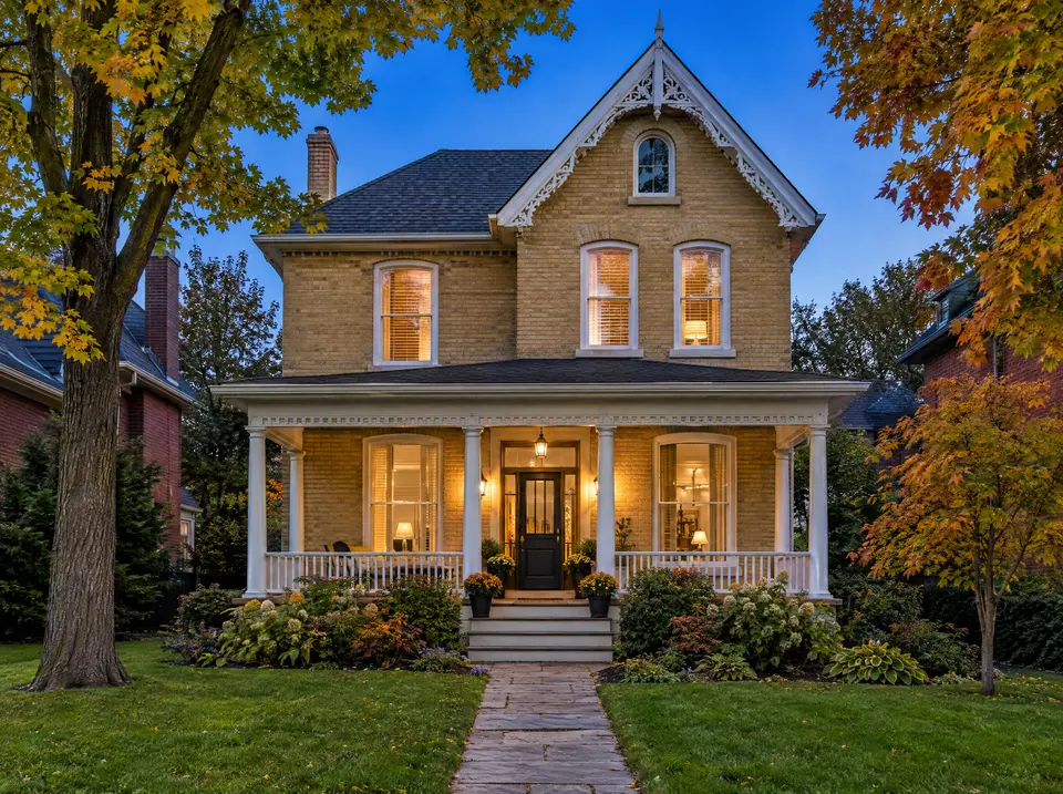 Yellow-brick Victorian home with gingerbread trim and wraparound porch in autumn