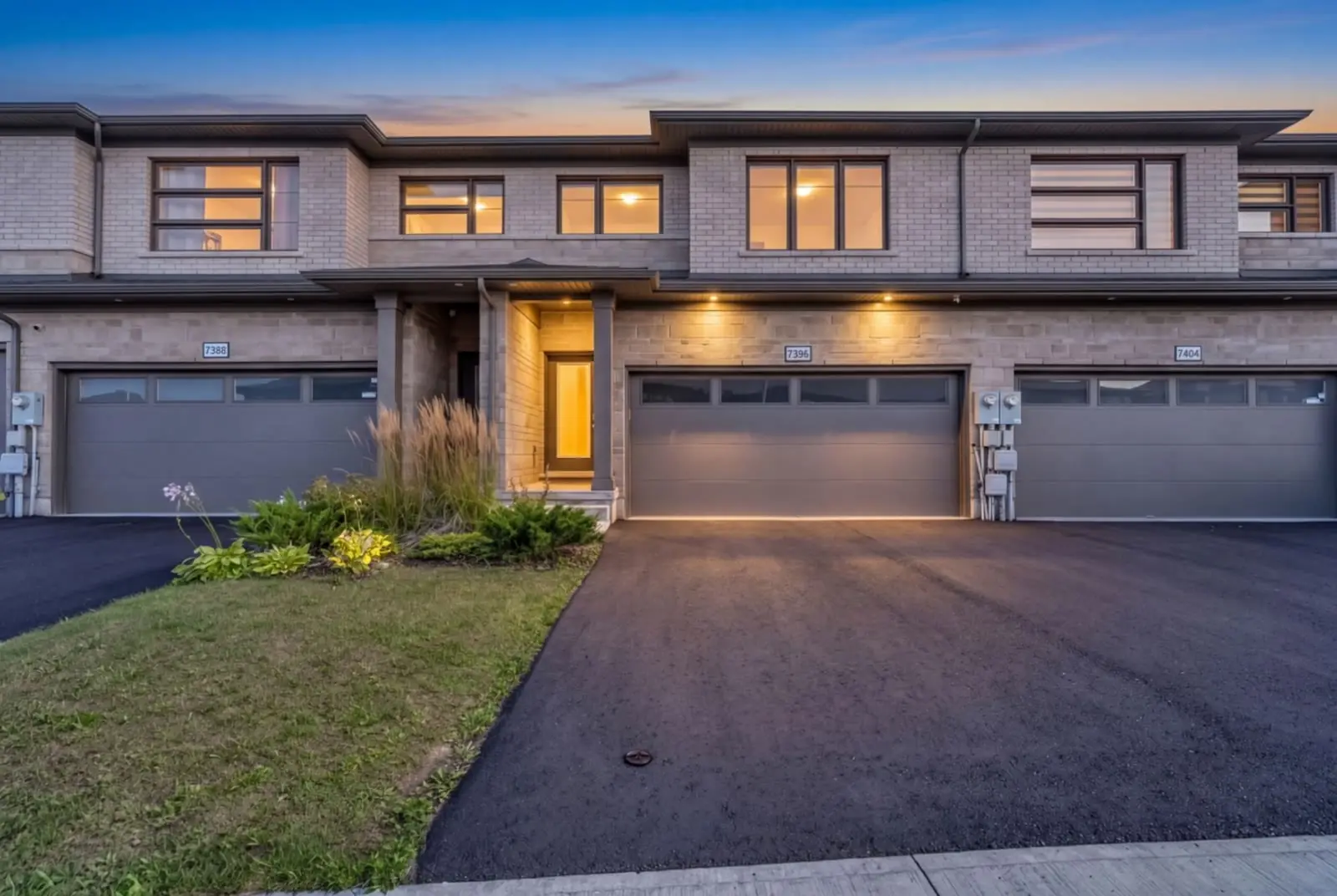 Modern townhomes in Niagara Falls at twilight, windows and garage lights on